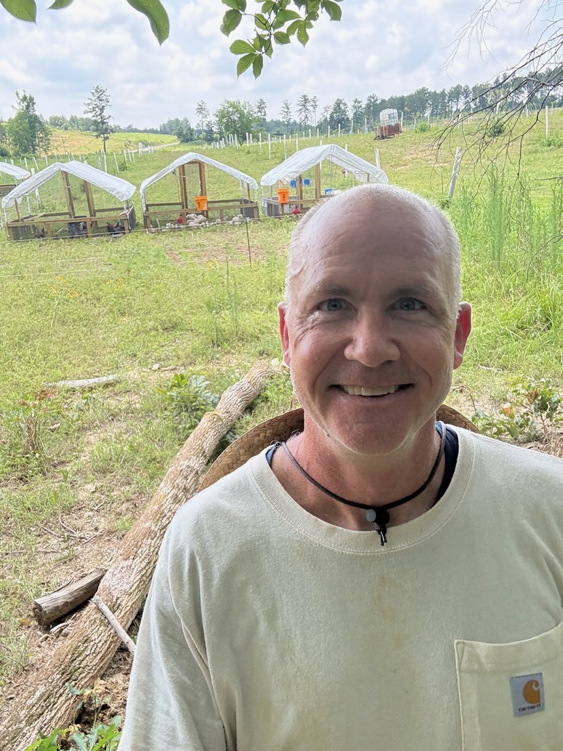 Rolf Versluis on his farm in Chatsworth, GA, with chicken coops and chestnut trees on the pasture behind him